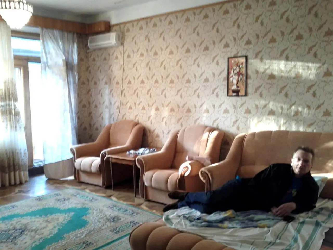 in this image this is a picture of a living room where we have a chandelier, curtain , door, air...